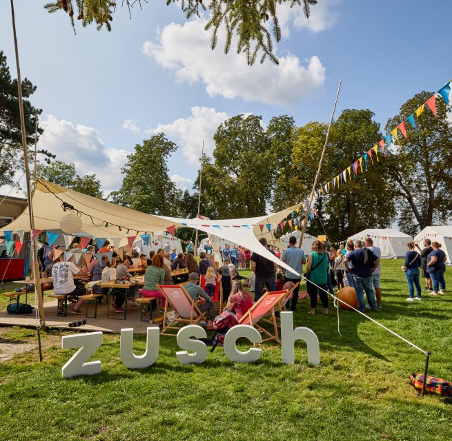 Mensen staan onder een luifel versierd met kleurrijke wimpels // © Oliver Borchert Mensen staan onder een luifel versierd met kleurrijke wimpels // © Oliver Borchert