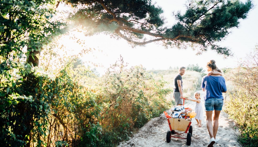 A family pulls a handcart with beach utensils barefoot towards the Baltic Sea beach in Dierhagen. // Summertime is family time - barefoot through the sand on the way to Dierhagen beach, with a picnic, bathing fun and lots of shared joy in your luggage. // © MV-T/Roth A family pulls a handcart with beach utensils barefoot towards the Baltic Sea beach in Dierhagen.