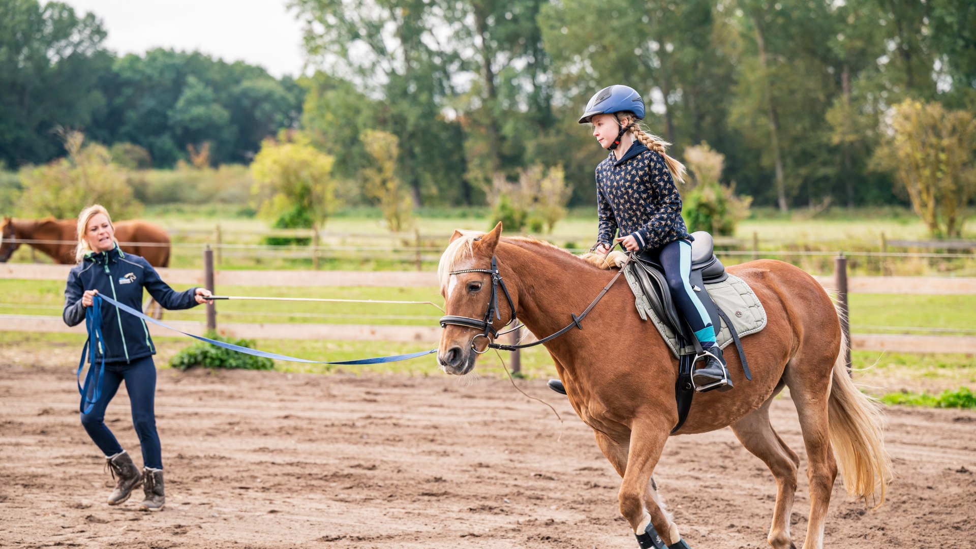 Een kind zit op een paard en wordt in een cirkel geleid door de rij-instructeur