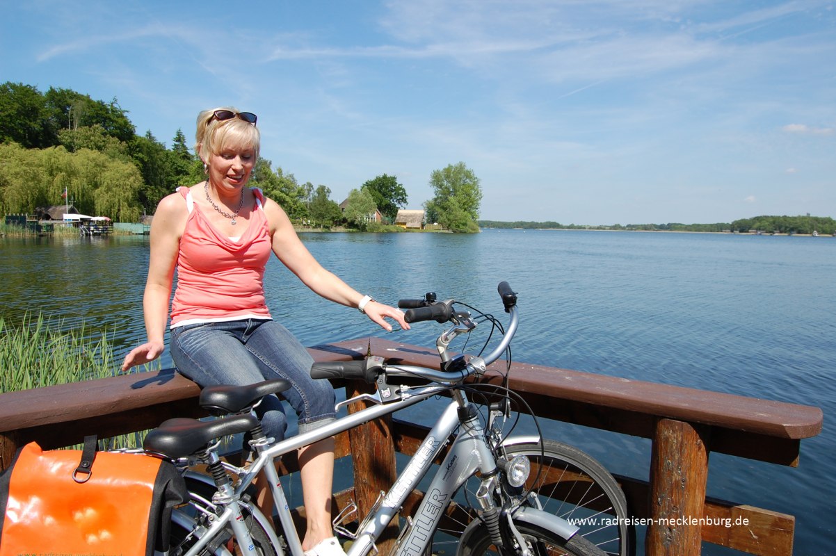 Rowerzysta siedzi na poręczy nad jeziorem. // © Ralf Tetmeyer, radreisen-mecklenburg Rowerzysta siedzi na poręczy nad jeziorem. // © Ralf Tetmeyer, radreisen-mecklenburg