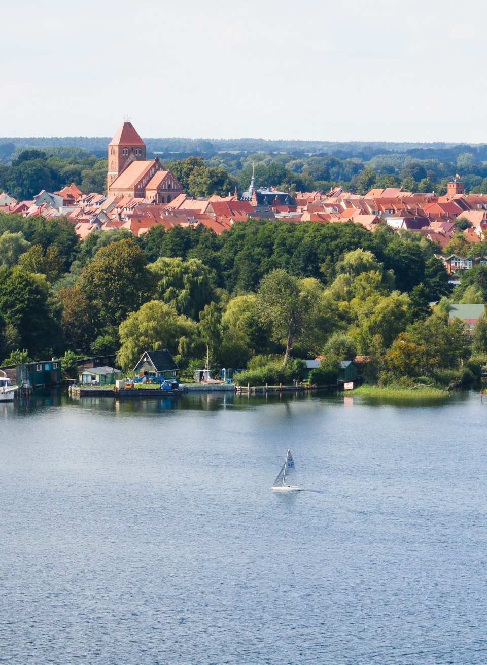 Een zeilboot op een meer en daarachter een stad met bakstenen gebouwen vanuit de lucht