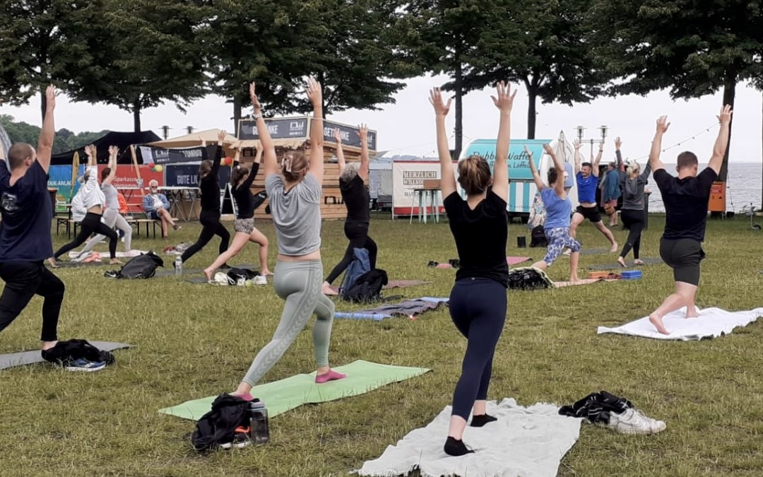 Een groep mensen doet yoga op de Hansawiese in Stralsund, direct aan het water, © MOVA PLACE - Yoga & Co. Studio