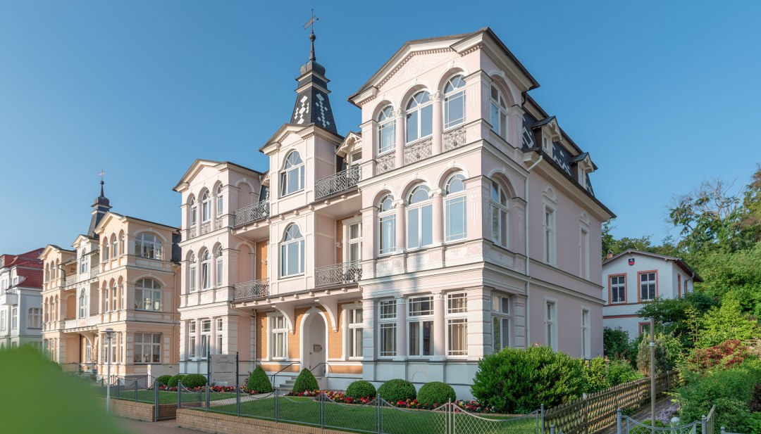 Historic spa villa in Ahlbeck on Usedom with ornate balconies and turrets under a bright blue sky.