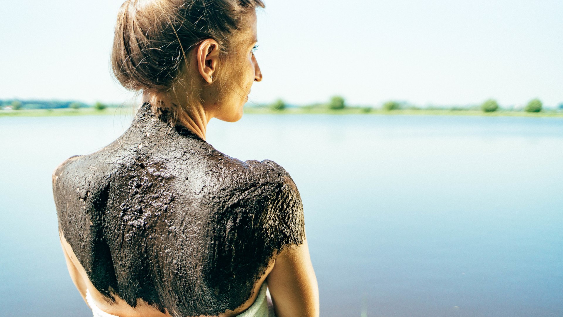 Mud pack on the back of a woman standing in the sun with a view of the water.
