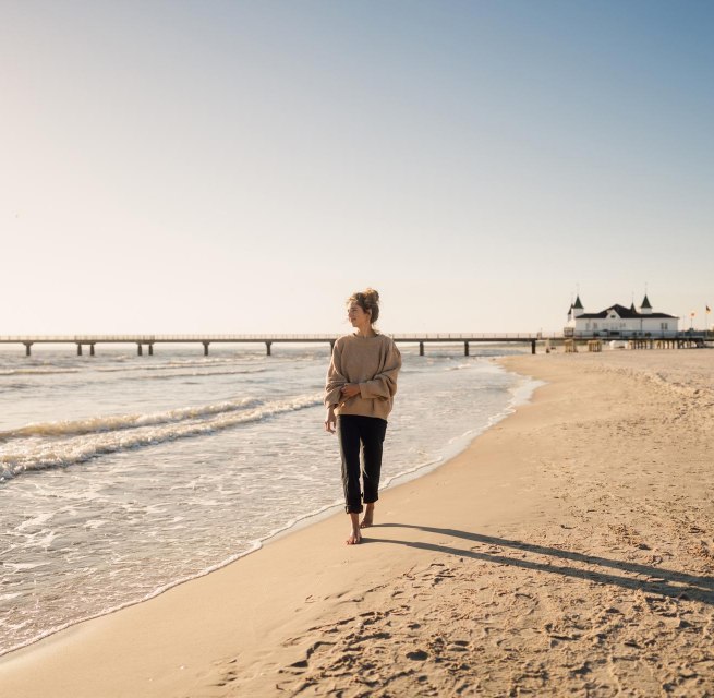 Woman walking on the beach of Ahlbeck at sunrise with pier in the background