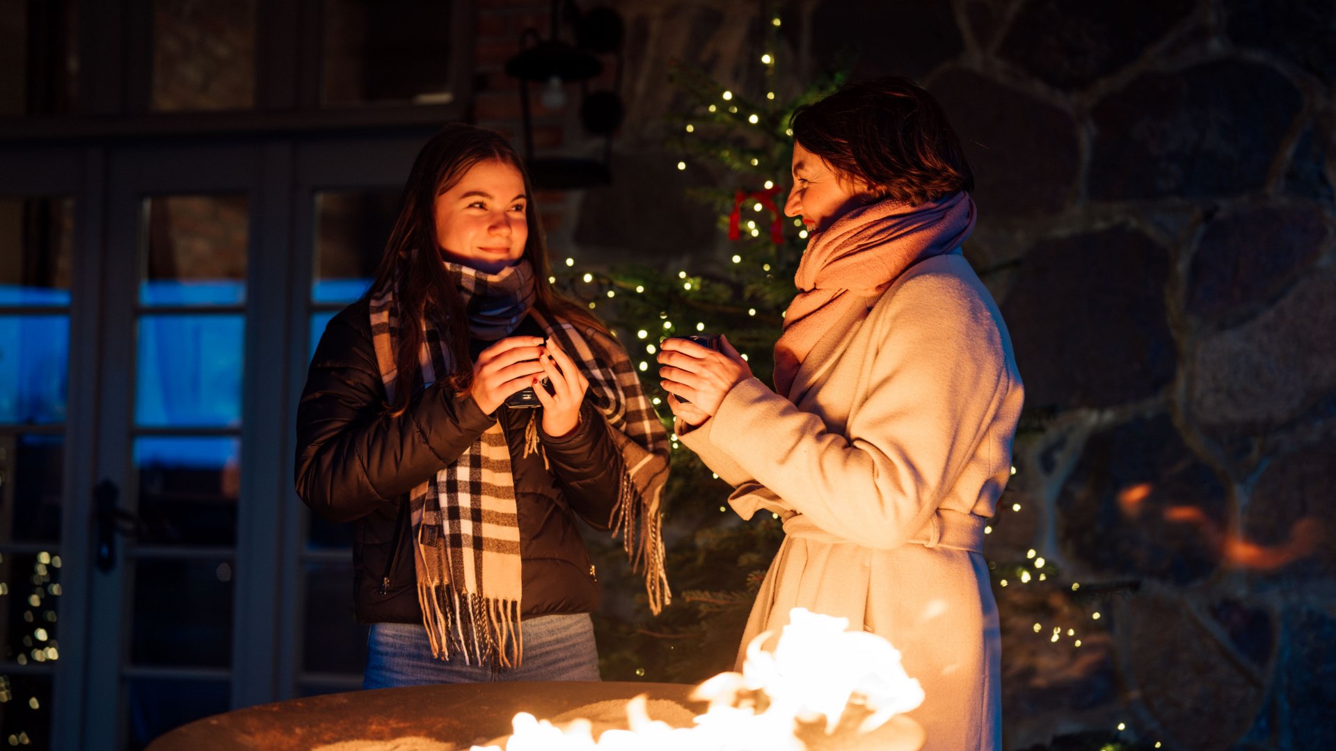 Twee vrouwen warmen zich bij een vuurschaal op de adventsmarkt in Slot Ulrichshusen, omringd door fonkelende lichtjes en een winterse sfeer.