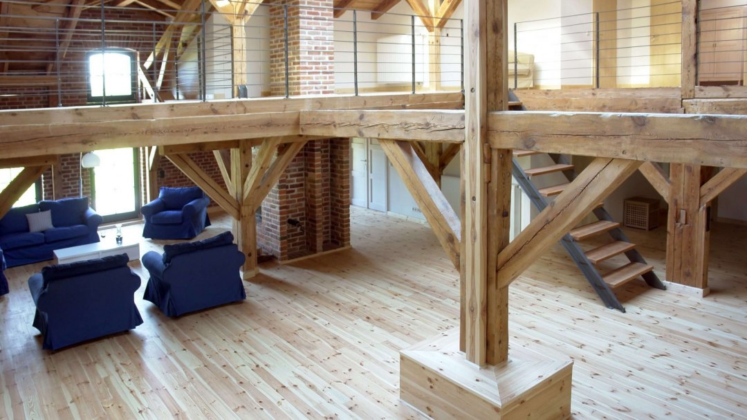 This stylish loft combines rustic charm with modern accents. The solid wooden beams and open-plan concept harmonize perfectly with the cosy seating areas, while the exposed brick walls preserve the historic character of the building. The spacious gallery offers additional room and emphasizes the airy atmosphere of this unique living space., © Dieses stilvolle Loft kombiniert rustikalen Charme mit modernen Akzenten. Die massiven Holzbalken und das offene Raumkonzept harmonieren perfekt mit den gemütlichen Sitzgelegenheiten, während die freiliegenden Ziegelwände den historischen Charakter des Gebäudes bewahren. Die großzügige Galerie bietet zusätzlichen Raum und betont die luftige Atmosphäre dieses einzigartigen Wohnraums.