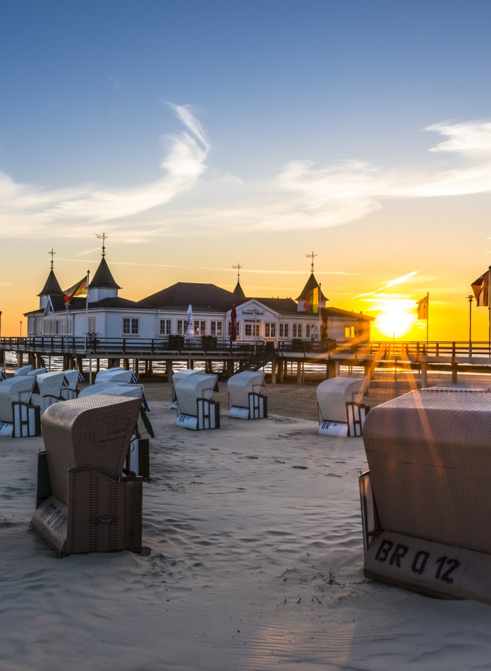 Sunrise on the Ahlbeck pier with beach chairs on the Baltic Sea beach and golden morning sun.