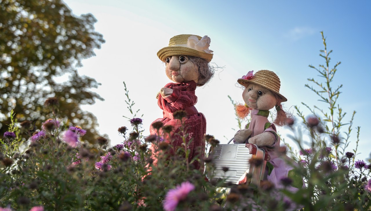 Hand puppet grandma and granddaughter in the garden in front of purple flowers, © info@maren-winter.de