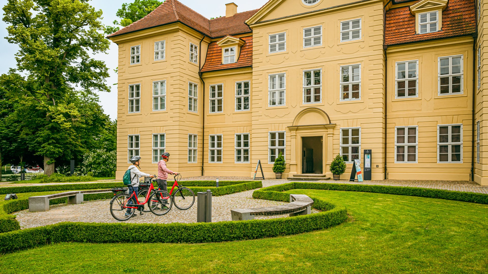 Een stel met e-bikes staat voor Mirow Castle // Het koninklijke eindpunt van de fietstocht is Kasteel Mirow. // © MV-T/Tiemann Een stel met e-bikes staat voor Mirow Castle