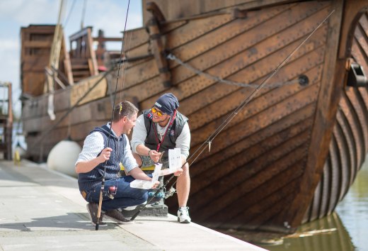Jonge mannen vissen in de haven van Ueckermünde met een tandrad op de achtergrond., © TMV/Läufer