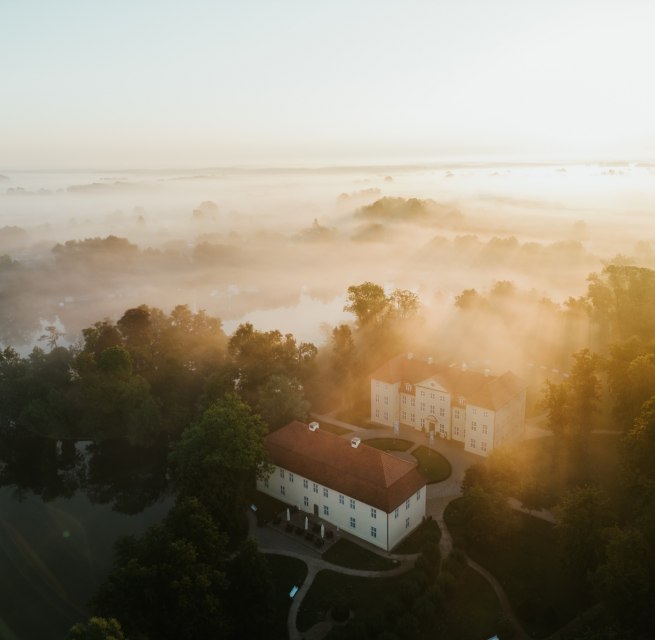 Goldenes Licht taucht Schloss Mirow in eine mystische Atmosph&auml;re. Nebelschwaden ziehen &uuml;ber die Seenlandschaft der Mecklenburgischen Seenplatte und lassen das historische Ensemble aus dem 18. Jahrhundert wie aus der Zeit gefallen wirken. Ein Moment purer Stille zwischen Wasser und Wald. // &copy; 1000seen.de