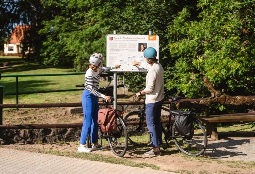 Twee fietsers staan bij het bord voor de Route van de Noord-Duitse Romantiek // Frauke en Wolf vinden op belangrijke punten langs de route informatie over de schilders en de regio. // © MV-T/Gross Twee fietsers staan bij het bord voor de Route van de Noord-Duitse Romantiek