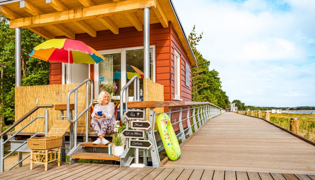 Een vrouw zit op de promenade bij haar kleine snackbar, waar ze ook strandstoelen verhuurt in Boltenhagen.