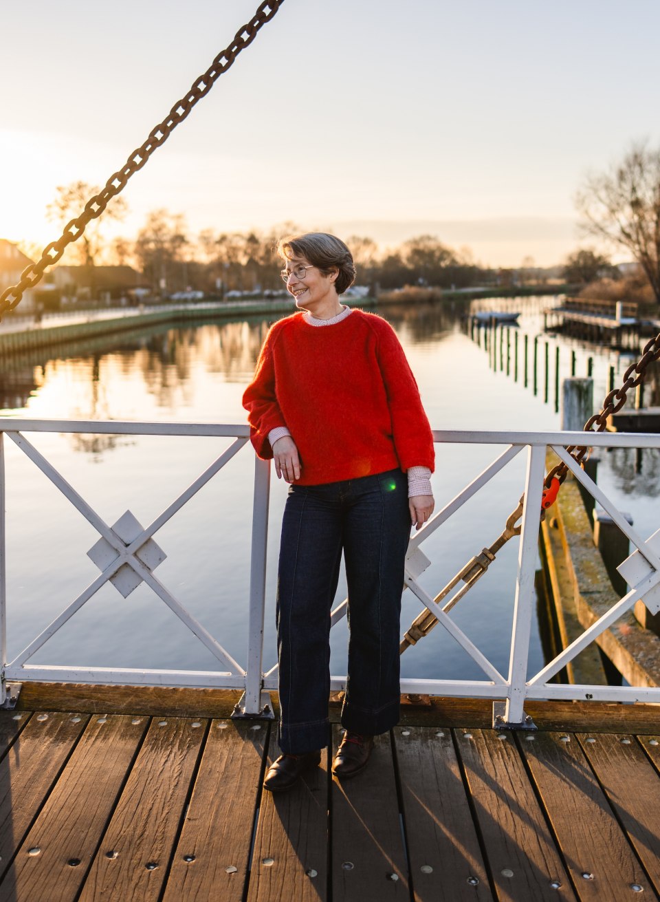 Vrouw op de witte Wiecker basculebrug bij zonsondergang, met de Ryck in Greifswald weerspiegeld op de achtergrond.