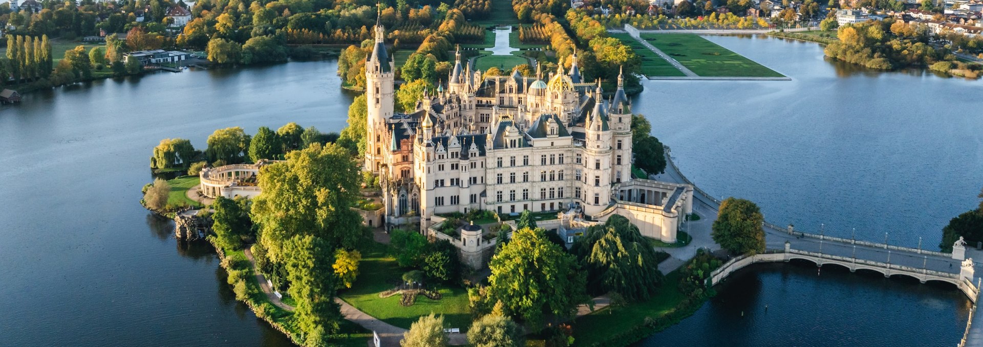 Widok z lotu ptaka na zamek w Schwerinie, otoczony wodą i jesiennymi drzewami o wschodzie słońca.