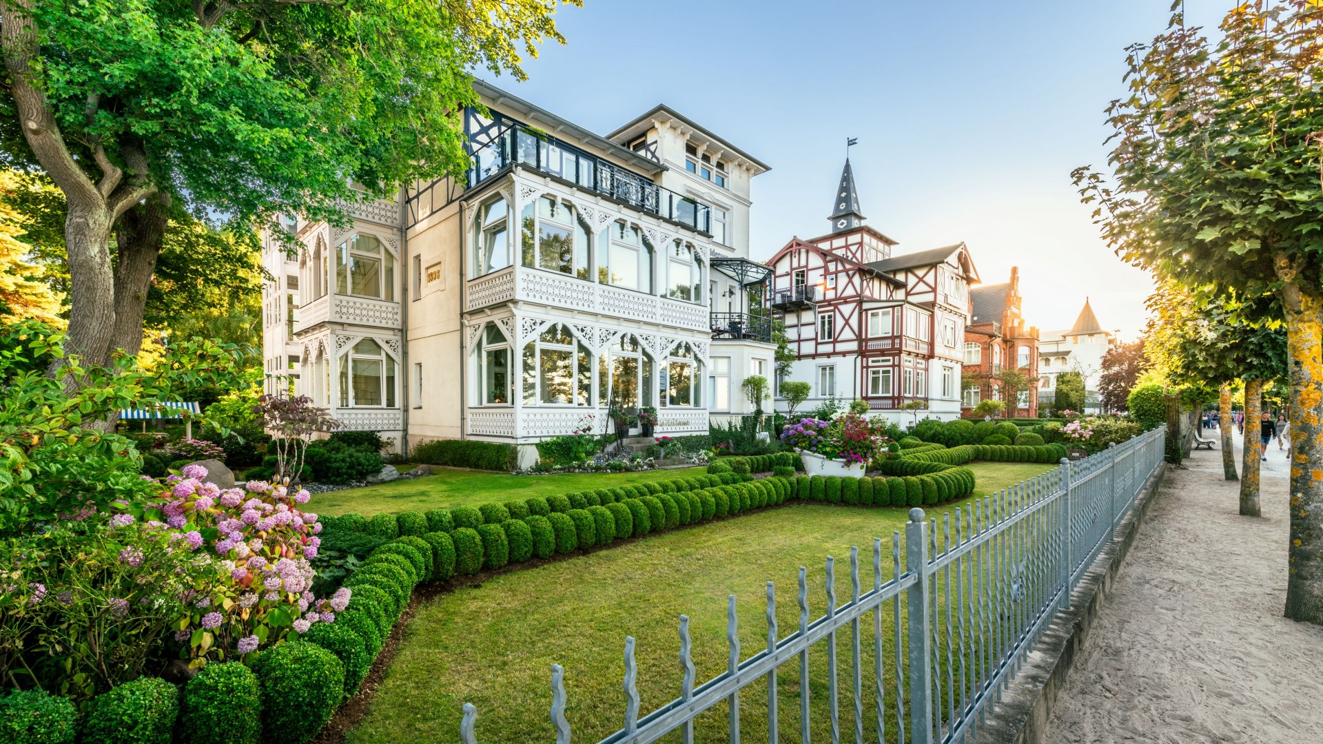 Historic villas with ornate facades and manicured gardens on a promenade with a sandy path.