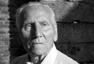 Black-and-white photograph: a man wearing a white shirt stands in front of a wall, looking serious // © Stefan Hanke Black-and-white photograph: a man wearing a white shirt stands in front of a wall, looking serious // © Stefan Hanke