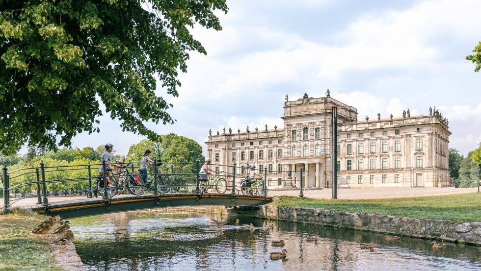 Discover the unique nature and culture in an environmentally friendly way on varied themed bike paths, such as the Residence Towns Circuit., © TMV/Tiemann A family with bicycles crosses the bridge with canal at Ludwigslust Castle